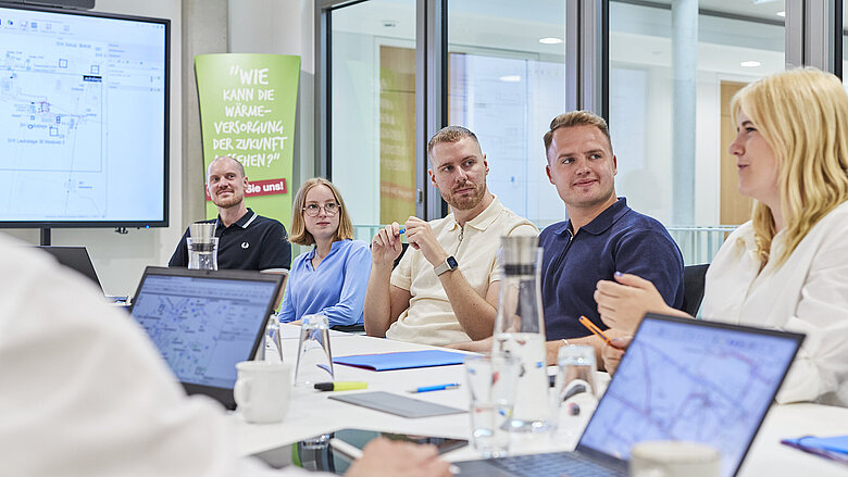 Fünf Beschäftigte in einer Besprechung am Konferenztisch mit Laptops und Präsentation