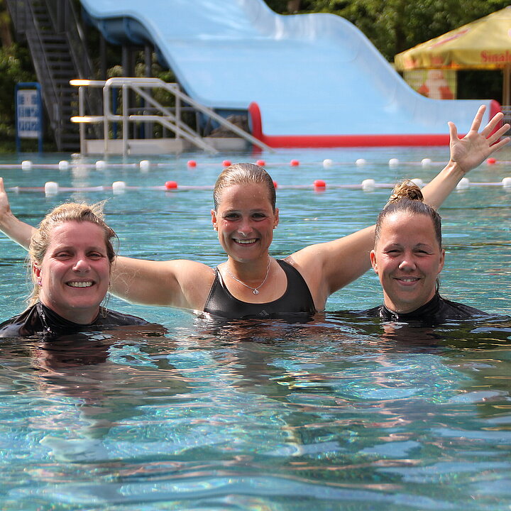 Drei Mitarbeiterinnen stehen mit erhobenen Armen im Freibad-Becken